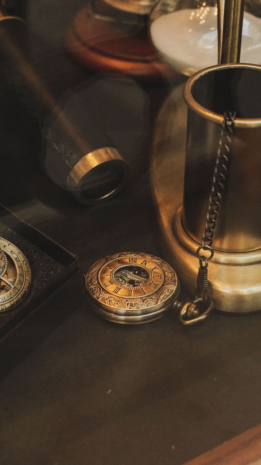 Engraved brass pocket watch with Roman numerals and open skeleton center resting beside a brass cup and chain