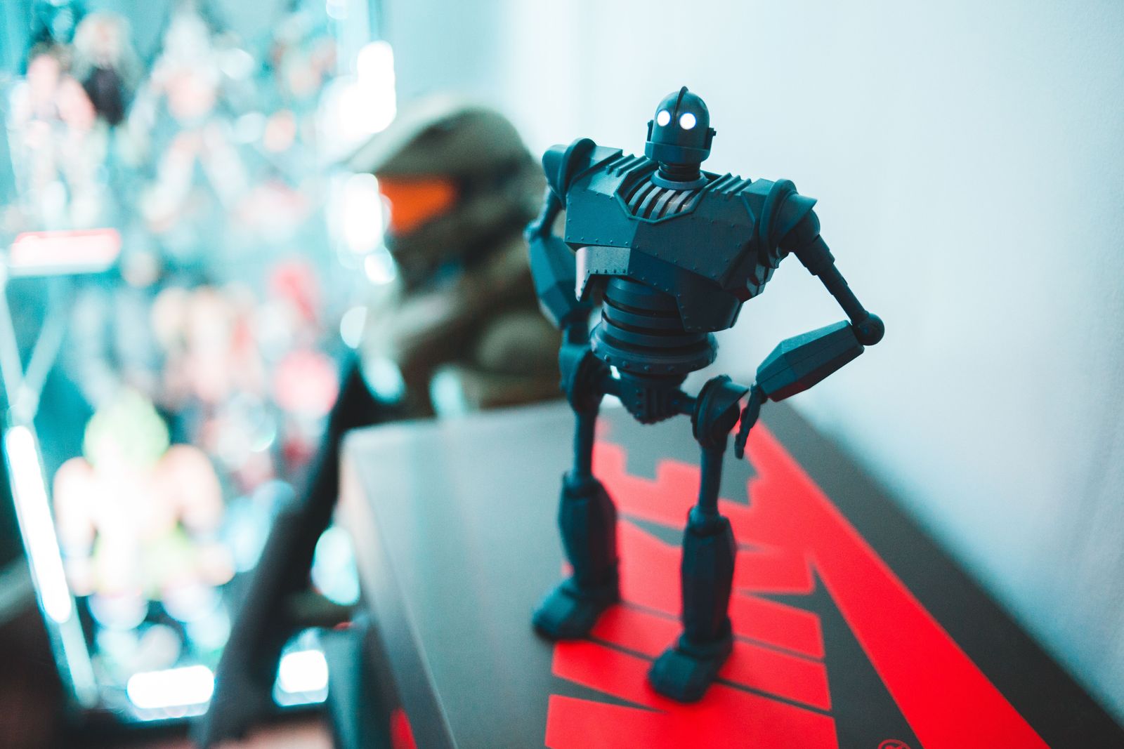 Dark grey riveted robot figure with glowing white eyes standing hand on hip on top of a red and black box
