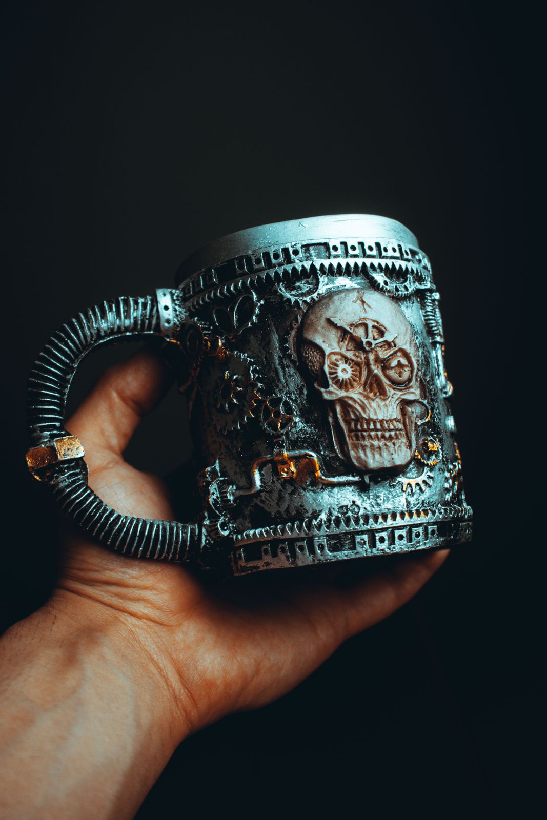 Hand holding a silver steampunk tankard sculpted with a gear-filled skull, cogs and a coiled pipe handle
